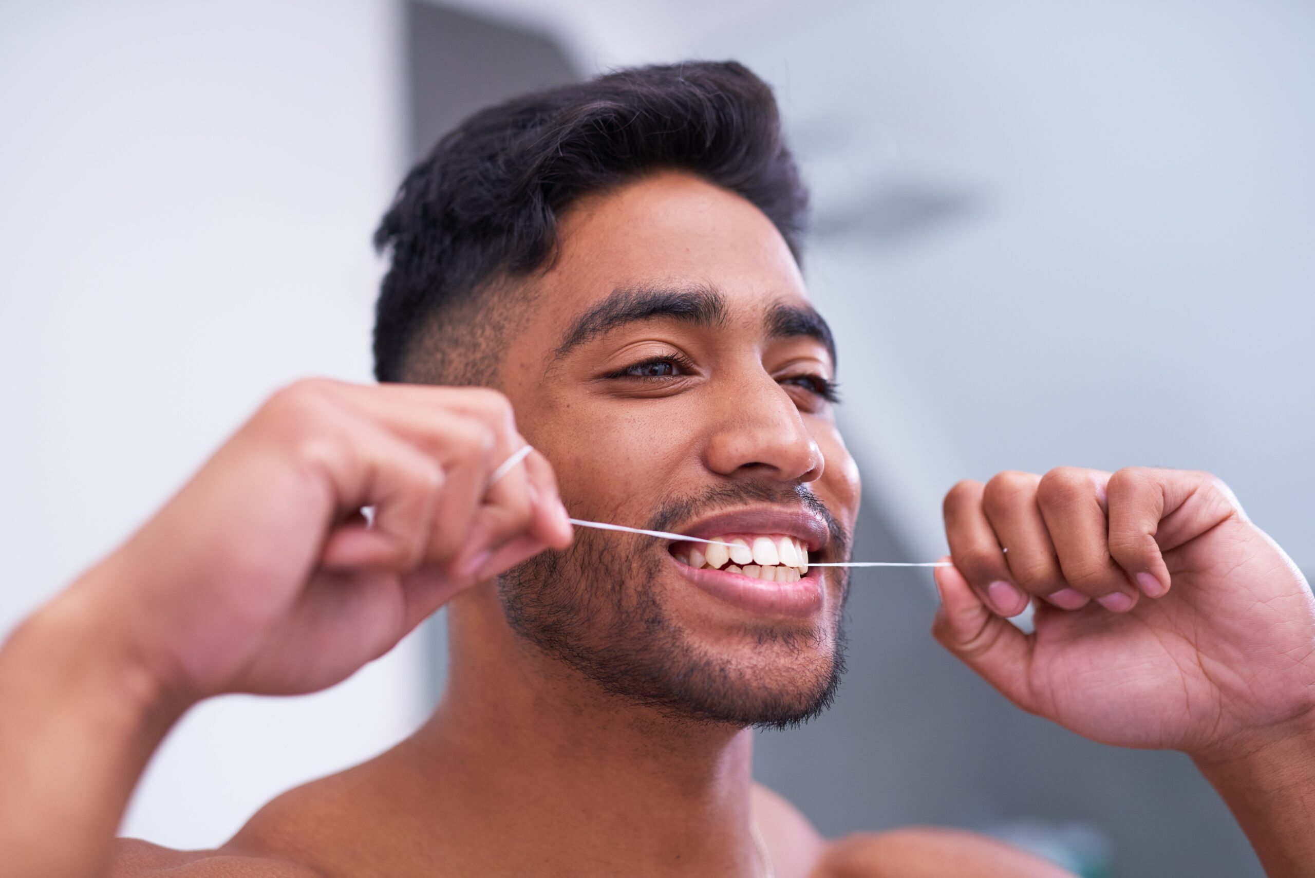 Shot of a handsome young man flossing his teeth in the bathroom at home
